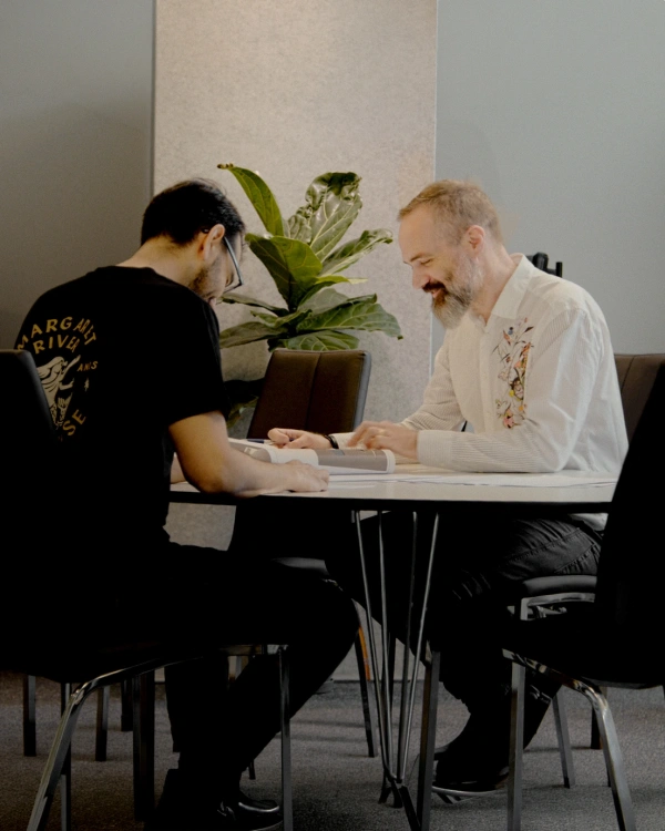 Två personer sitter vid ett bord och diskuterar ritningar och projektdokument.